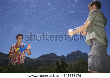 Two teenage boys fighting with water guns in mountains