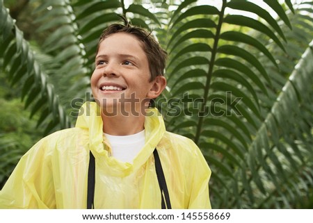 Happy young boy in raincoat standing in front of large fern during field trip