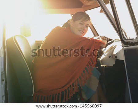 Portrait of happy young woman wrapped in shawl sitting at driver\'s seat of van