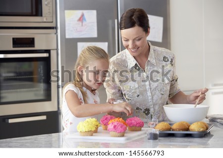 Happy mother and daughter preparing cupcakes in kitchen