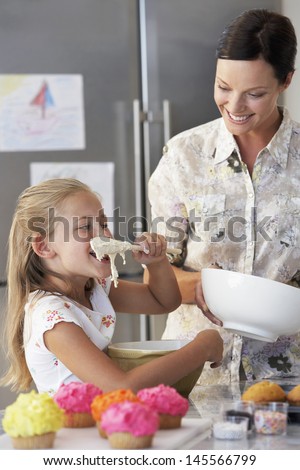 Happy mother with daughter tasting cupcake batter in kitchen