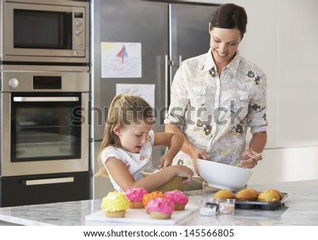 Happy mother and daughter making cupcakes in kitchen