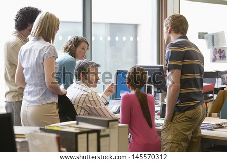 Rear view of a group of multiethnic office workers around colleague using computer