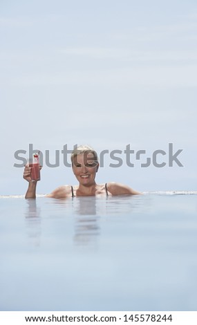 Portrait of happy middle aged woman holding daiquiri in infinity pool
