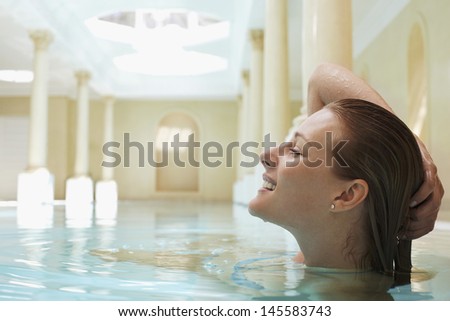 Side view of smiling young woman with hand on head in swimming pool