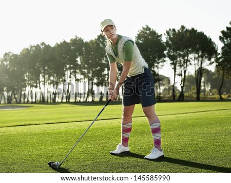 Full length of young female golfer teeing off on golf course