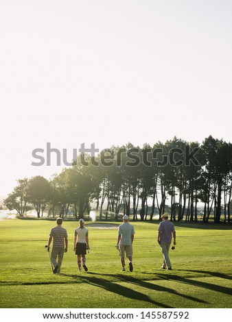 Rear view of young golfers walking on golf course