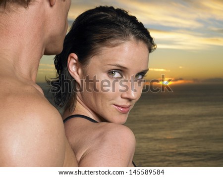 Closeup of a woman looking over shoulder with man behind her at sunset over ocean