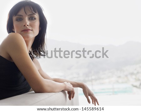 Portrait of a beautiful young woman leaning on couch against blurred mountains