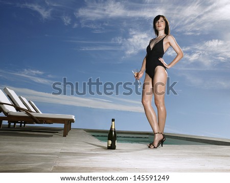 Low angle view of a young woman in bathing suit holding champagne at poolside