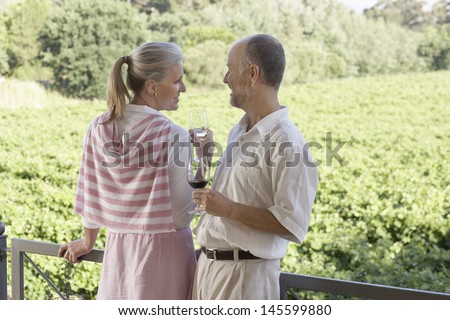 Happy middle aged couple holding wine glasses in front of vineyard