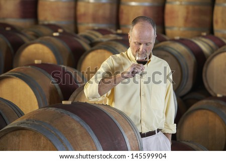 Middle aged man tasting red wine surrounded by barrel in cellar
