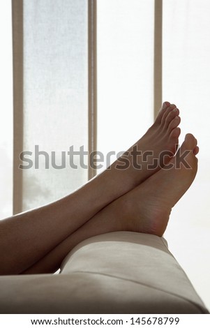 Low section of woman resting with feet up on sofa in living room