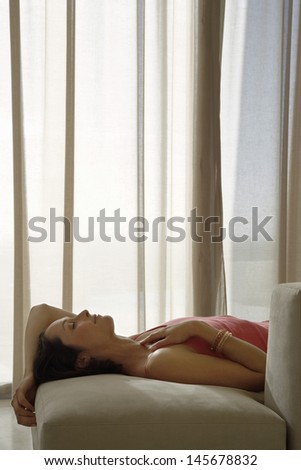 Side view of relaxed woman lying on sofa in living room