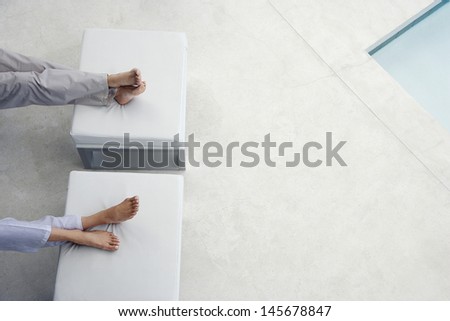 Low section of couple sitting with feet on foot stools by swimming pool Low section of couple sitting with feet on foot stools by swimming pool