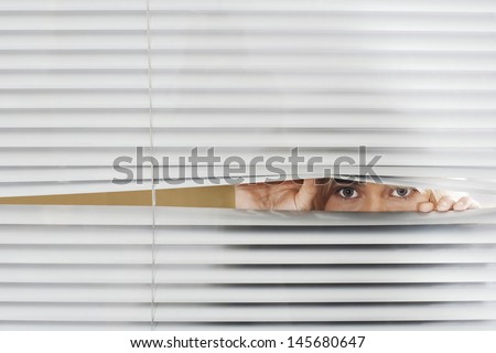 Young woman looking through Venetian blinds