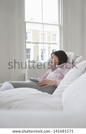Young woman sleeping on couch with remote control in hand