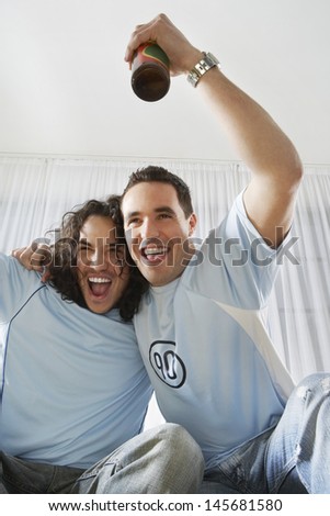 Two young men cheering while watching television with beer bottle