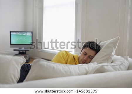 Young man sleeping on couch with television in background