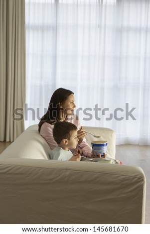 Side view of mother and son watching television while eating icecream at home