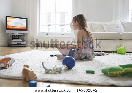 Side View Of A Little Girl Watching Television With Toys On Floor