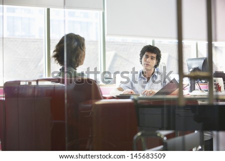 View through glass wall of businessman and woman in meeting