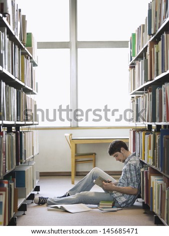 Side view of a young male college student reading in the library