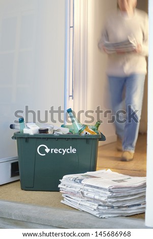Closeup of recycling container and pile of waste papers on floor with blurred person in background