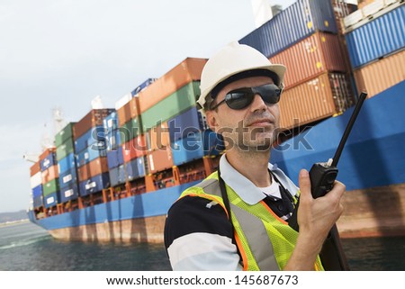Man in hard hat using walkie talkie at container terminal