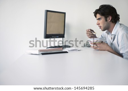 Side view of a young businessman eating while sitting at office desk