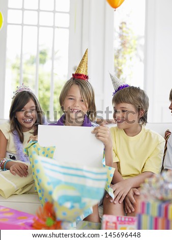 Three children at birthday party as one open the gift