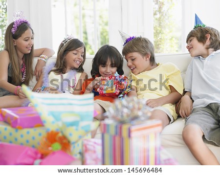 Children sitting on sofa at birthday party as one open the gift