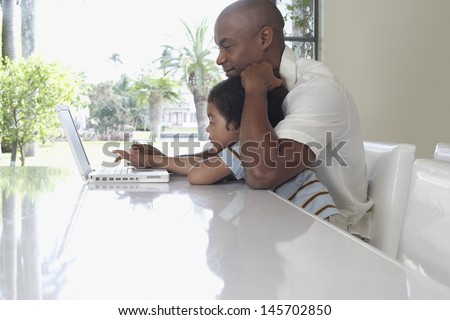 Side view of father and son using laptop at dining table