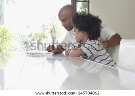 Side View Of Father And Son Using Laptop At Dining Table