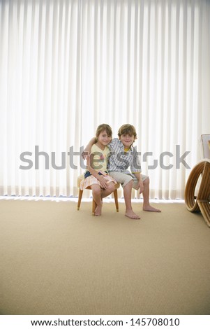 Full length portrait of little brother and sister sitting on stool in front of curtains