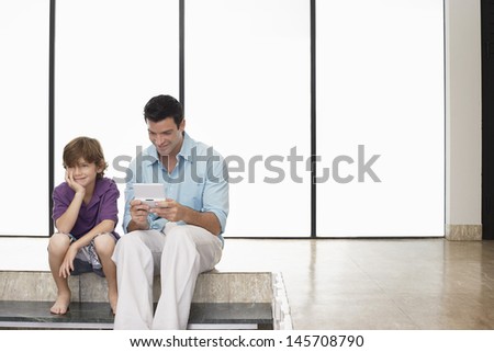 Happy father playing handheld video game sitting next to son at home