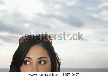 Closeup of teenage girl with sunglasses on top of head against cloudy sky