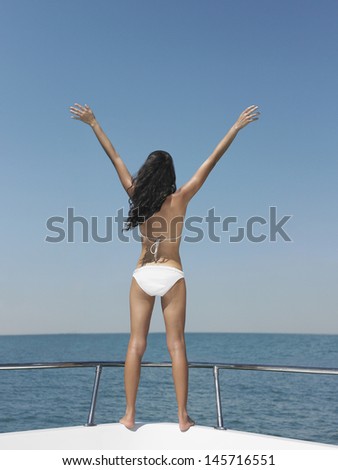Rear view of young woman in bikini with arms outstretched on bow of yacht
