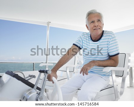 Happy middle aged man sitting at helm of luxury yacht