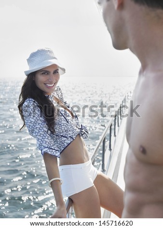Beautiful young woman flirting with shirtless man on yacht