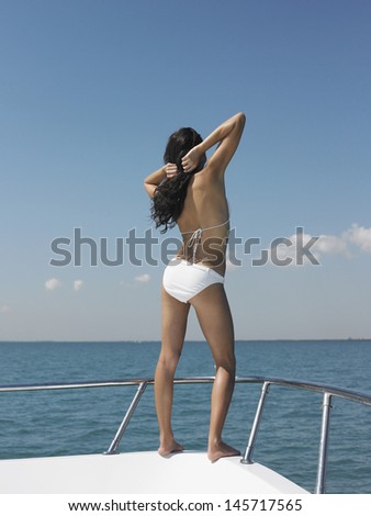 Full length rear view of young woman in bikini standing on bow of yacht