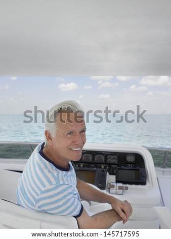 Smiling middle aged man sitting at helm of luxury yacht