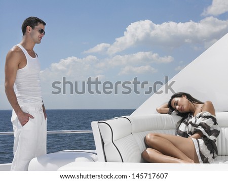 Young man looking at woman sleeping on sofa in luxury yacht