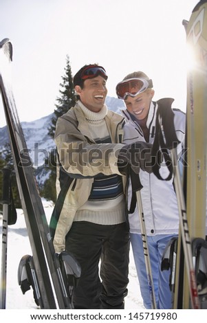 Cheerful skiing couple in warm clothing with skis against mountains
