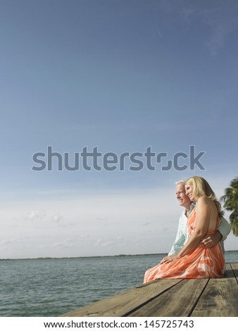 Side view of a middle aged couple sitting on edge of pier