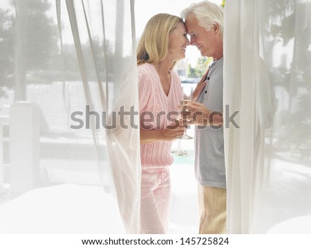 Side view of a middle aged couple with champagne flutes behind curtain