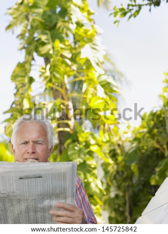 Relaxed mature man reading newspaper against plants outdoors