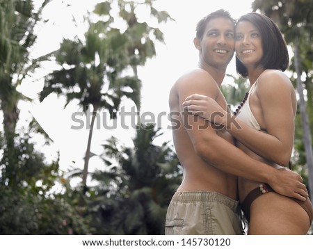 Side view of a semi dressed young couple standing against trees and sky