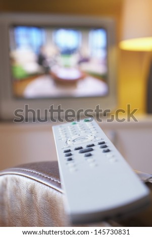 Remote control on leather armchair with television in background