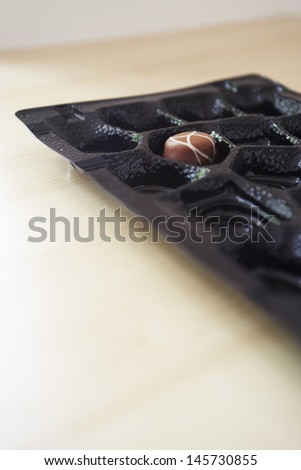 Chocolate box on wooden table with only one truffle remaining